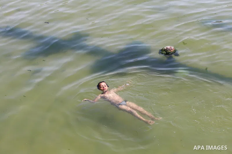 A Palestinian youth swims into the Mediterranean Sea as he enjoys a warm day at the seaport in Gaza City on May 25, 2015. Photo by Mohammed Asad