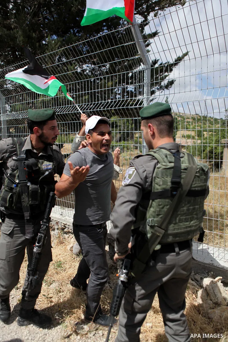 Israeli security try to stop a Palestinian protester from placing the national flag on the fence of al-Barak building, near al-Aroub Palestinian refugee camp, just north the West Bank town of Hebron on May 30, 2015, duri...