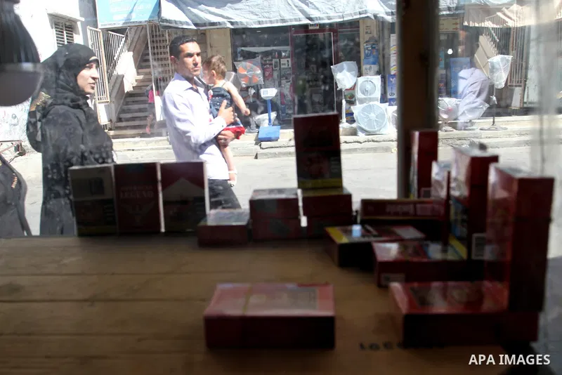 A Palestinian man with his wife walks past a vendor selling cigarettes in the southern Gaza Strip City of Rafah, on May 31, 2015. Smuggling through tunnels began several months after Islamic Hamas movement's control of t...