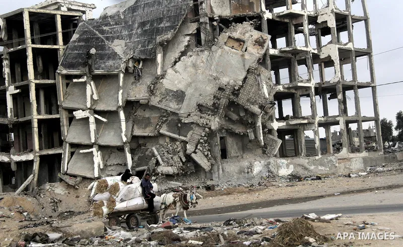 Palestinians ride a donkey cart in front of the remains of houses, which were destroyed during the 50-day Israeli war in the summer of 2014, in Beit Lahia in the northern Gaza Stip, June 1, 2015. Photo by Nidal Alwaheidi