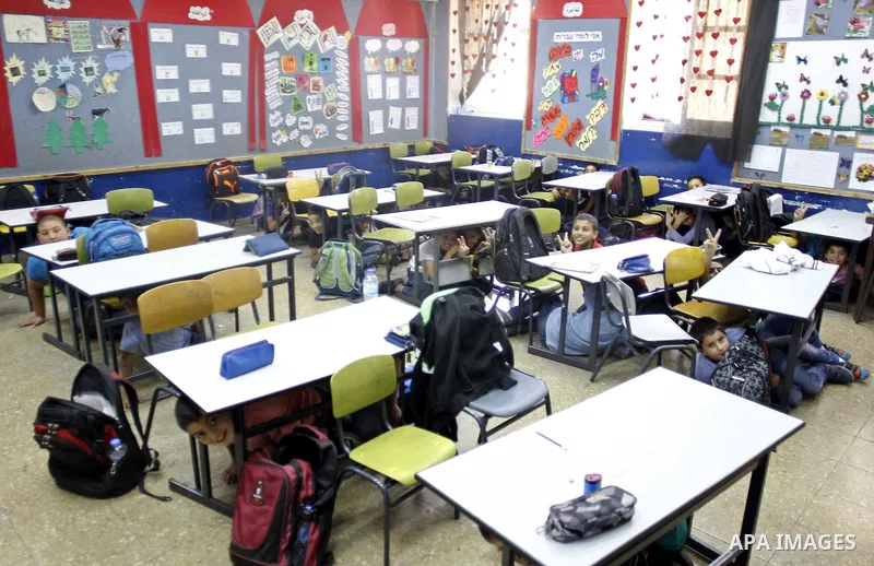 Israeli-Arab schoolchildren sit unde tables at a school in Jerusalem after sirens sounded across Israel as part of country-wide massive civil defence exercise aimed at preparing the country for air or missile attacks inv...