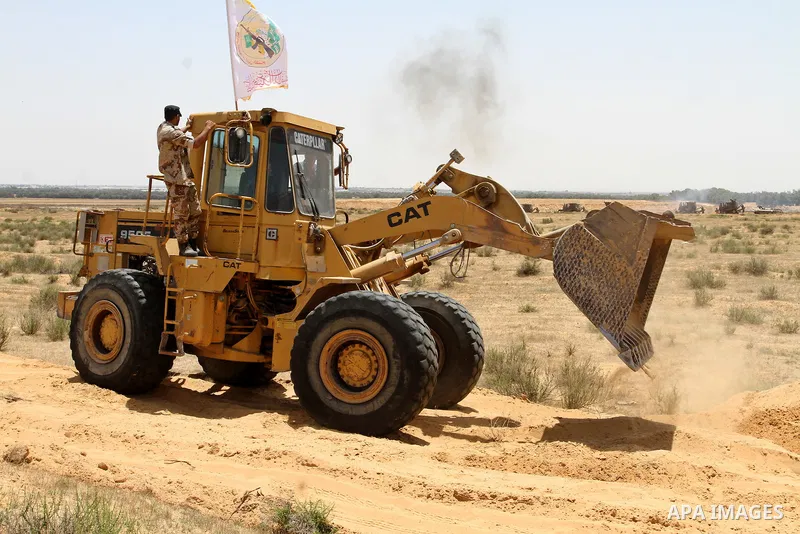 A Palestinian militant of the Ezzedine al-Qassam Brigades, Hamas' armed wing, rides a bulldozer in front of Israeli bulldozers working along a barbed wire fence that separates Rafah in the southern Gaza Strip and the Isr...