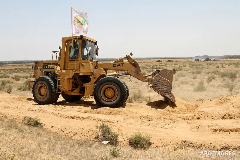 A Palestinian militant of the Ezzedine al-Qassam Brigades, Hamas' armed wing, rides a bulldozer in front of Israeli bulldozers working along a barbed wire fence that separates Rafah in the southern Gaza Strip and the Isr...