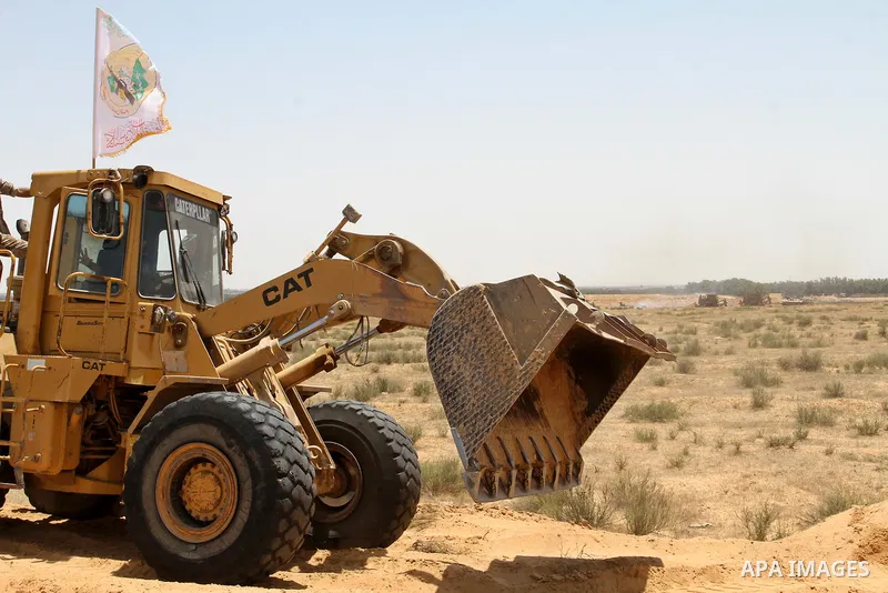 A Palestinian militant of the Ezzedine al-Qassam Brigades, Hamas' armed wing, rides a bulldozer in front of Israeli bulldozers working along a barbed wire fence that separates Rafah in the southern Gaza Strip and the Isr...