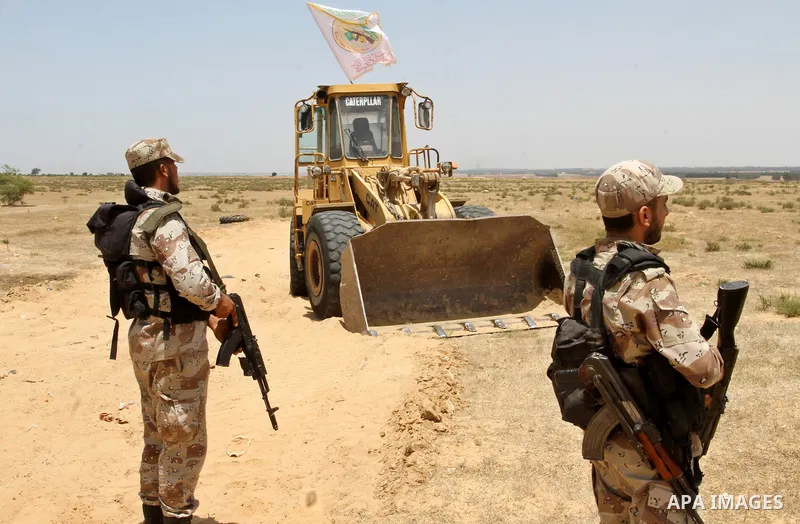 Palestinian militants of the Ezzedine al-Qassam Brigades, Hamas' armed wing, stand near a Palestinian bulldozer as they watch an Israeli bulldozers working along a barbed wire fence that separates Rafah in the southern G...