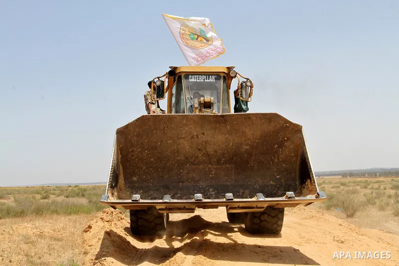 A Palestinian militant of the Ezzedine al-Qassam Brigades, Hamas' armed wing, rides a bulldozer in front of Israeli bulldozers working along a barbed wire fence that separates Rafah in the southern Gaza Strip and the Isr...