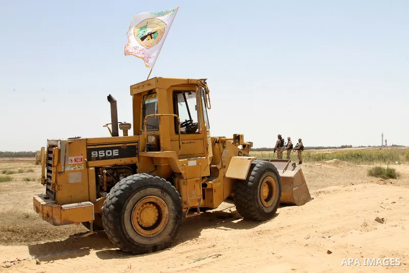 Palestinian militants of the Ezzedine al-Qassam Brigades, Hamas' armed wing, stand near a Palestinian bulldozer as they watch an Israeli bulldozers working along a barbed wire fence that separates Rafah in the southern G...