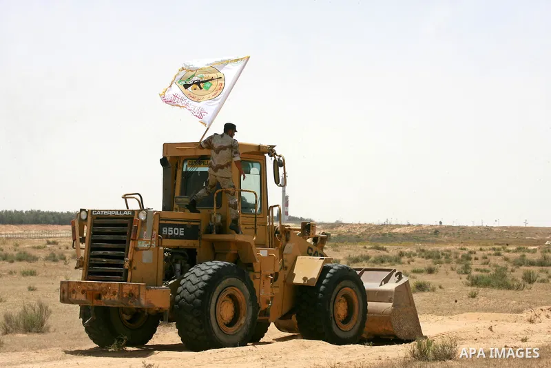 A Palestinian militant of the Ezzedine al-Qassam Brigades, Hamas' armed wing, rides a bulldozer in front of Israeli bulldozers working along a barbed wire fence that separates Rafah in the southern Gaza Strip and the Isr...