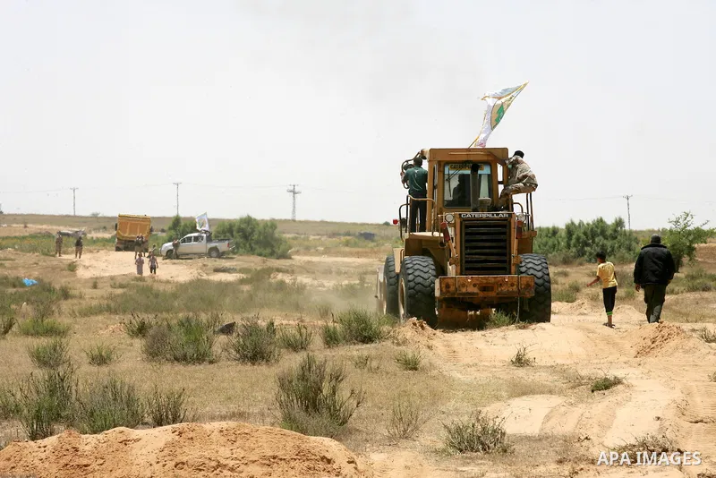 A Palestinian militant of the Ezzedine al-Qassam Brigades, Hamas' armed wing, rides a bulldozer in front of Israeli bulldozers working along a barbed wire fence that separates Rafah in the southern Gaza Strip and the Isr...