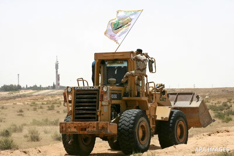 A Palestinian militant of the Ezzedine al-Qassam Brigades, Hamas' armed wing, rides a bulldozer in front of Israeli bulldozers working along a barbed wire fence that separates Rafah in the southern Gaza Strip and the Isr...
