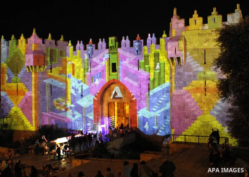 People watch an audiovisual light show projected over the ancient walls of Jerusalem's Damascus Gate in the old city during the Festival of Lights, on June 4, 2015. The festival is an annual event where thousands take pa...