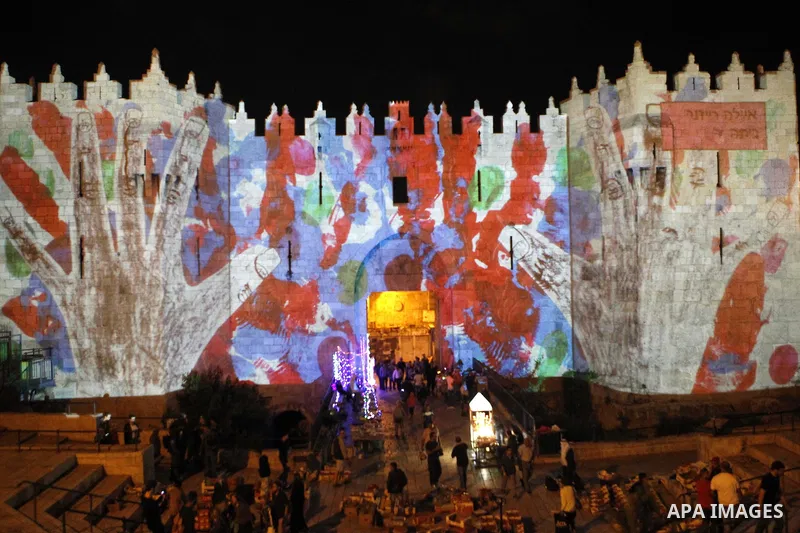 People watch an audiovisual light show projected over the ancient walls of Jerusalem's Damascus Gate in the old city during the Festival of Lights, on June 4, 2015. The festival is an annual event where thousands take pa...