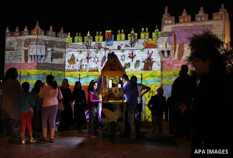 People watch an audiovisual light show projected over the ancient walls of Jerusalem's Damascus Gate in the old city during the Festival of Lights, on June 4, 2015. The festival is an annual event where thousands take pa...
