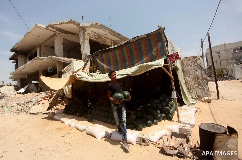 Palestinian vendor sells watermelon near the rubble of houses which were destroyed during the 50-day war between Israel and Hamas militants in the summer of 2014, in the Al-Shaaf neighbourhood, on June 06, 2015. Qatar's...