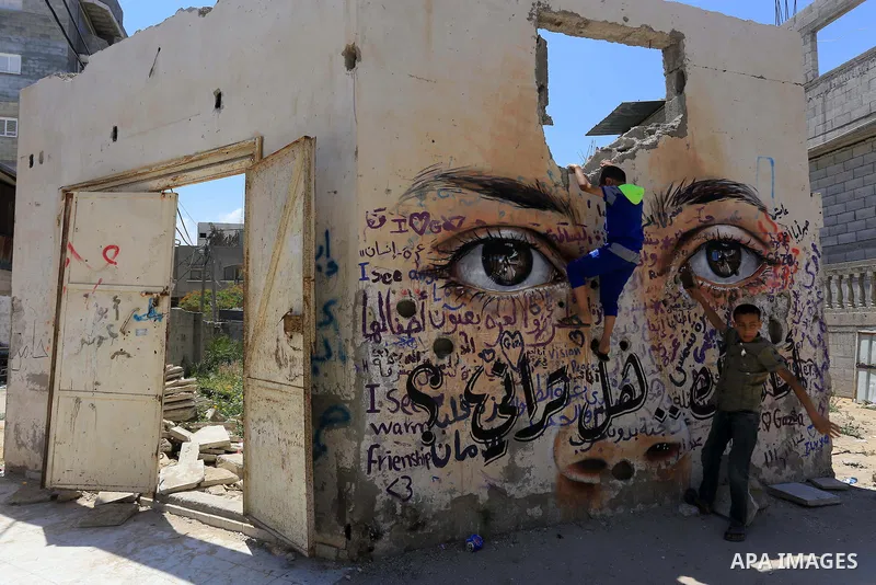 Palestinian boys play over a wall painted with a mural by German artist Akot on the walls of houses destroyed during the 50-day Israeli offensive on the Gaza Strip in last July and August in Gaza City on June 11, 2015. P...