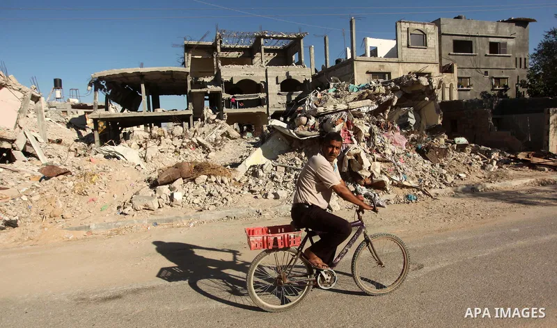 A Palestinian man rides a bicycle past rubble of buildings that were destroyed during 50-day Israeli on Gaza Strip in the summer of 2014, east of Khan Younis in the southern Gaza Strip on June 22, 2015. A widely anticipa...