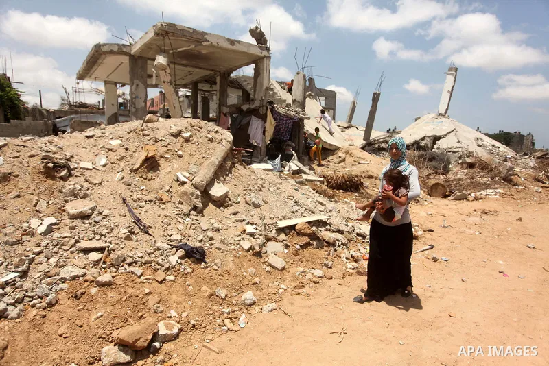 A Palestinian woman holds her daughter as she walks past the ruins of houses, that witnesses said were destroyed by Israeli shelling during a 50-day war last summer, in Khan Younis in the southern Gaza Strip July 2, 2015...