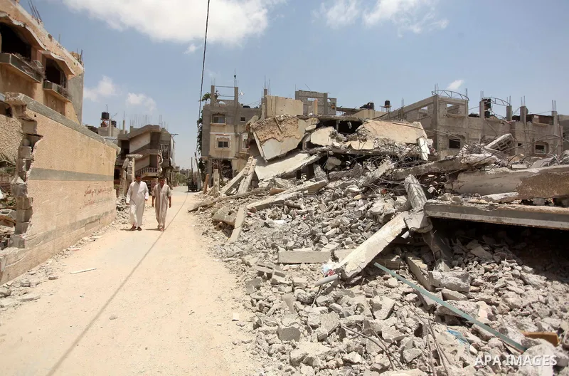 Palestinians walks past the ruins of houses, that witnesses said were destroyed by Israeli shelling during a 50-day war last summer, in Khan Younis in the southern Gaza Strip July 2, 2015. Robert Turner has no quick and...
