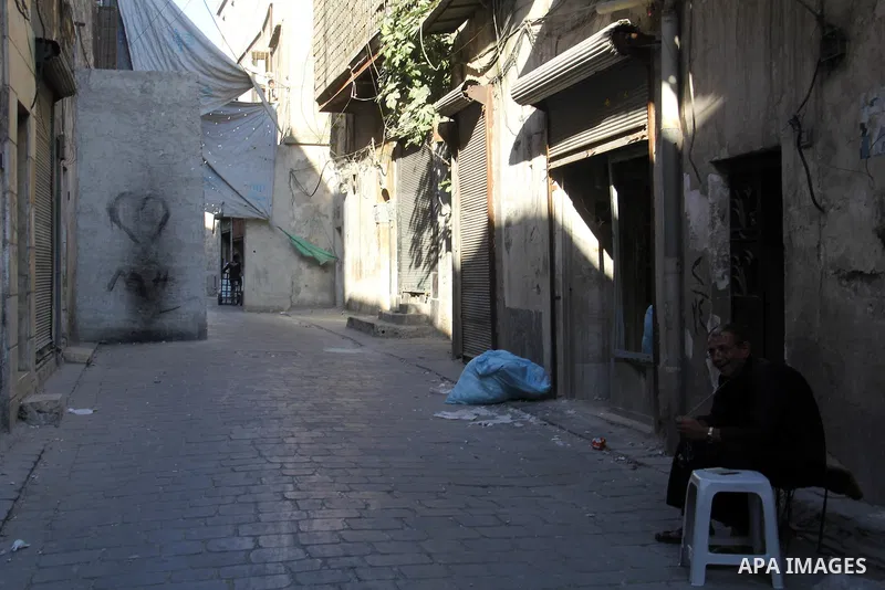 A Syrian man sits at the street in the northern Syrian city of Aleppo on July 05, 2015. The Syrians used the wreckage buses, cars and concrete slabs to protect themselves from the snipers of Syrian regime forces. Photo b...
