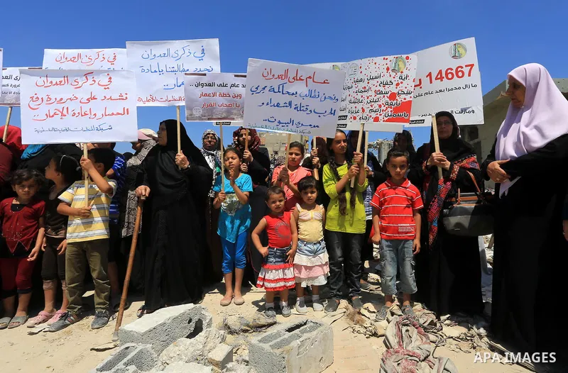 Palestinian women hold placards denouncing the 50-day war between Israel and Hamas' militants in the summer of 2014, and calling for the lift of the Israeli-imposed siege on the Gaza Strip, on July 7, 2015, during a demo...