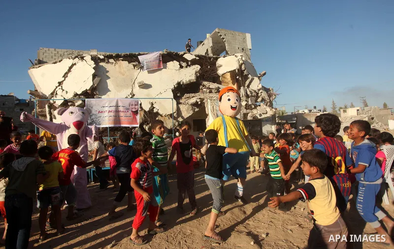 Palestinians wearing costumes perform to amuse children in front of a house, that witnesses said was destroyed by Israeli shelling during a 50-day war last summer, in the east of Gaza City July 8, 2015. The majority of c...