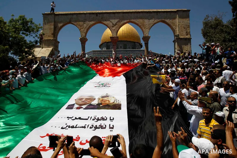 Palestinian Muslim worshippers hold a big version of their national flag bearing pictures of late Palestinian leader Yasser Arafat and current leader Mahmud Abbas during a demonstration to mark the Quds (Jerusalem) day f...