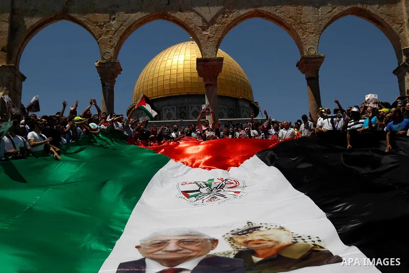 Palestinian Muslim worshippers hold a big version of their national flag bearing pictures of late Palestinian leader Yasser Arafat and current leader Mahmud Abbas during a demonstration to mark the Quds (Jerusalem) day f...