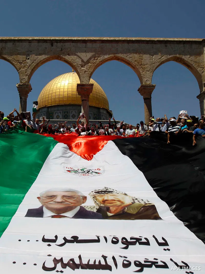 Palestinian Muslim worshippers hold a big version of their national flag bearing pictures of late Palestinian leader Yasser Arafat and current leader Mahmud Abbas during a demonstration to mark the Quds (Jerusalem) day f...