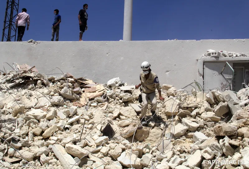 Syrians watch as rescue workers remove the debris of a building after two days of a reported bomb barrel attack by Syrian government forces, in Sheikh Khadr rebel held district in the northern Syrian city of Aleppo, June...