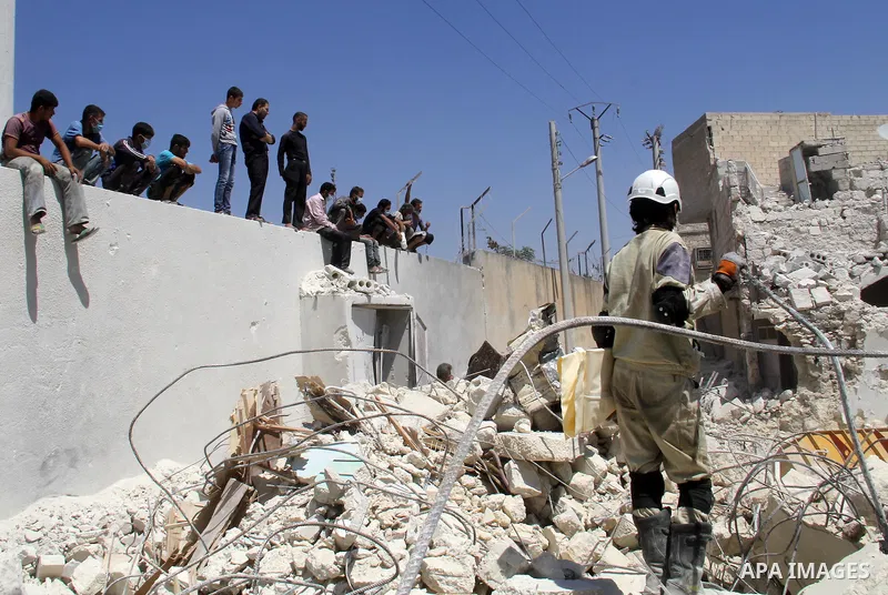 Syrians watch as rescue workers remove the debris of a building after two days of a reported bomb barrel attack by Syrian government forces, in Sheikh Khadr rebel held district in the northern Syrian city of Aleppo, June...