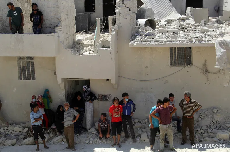 Syrians watch as rescue workers remove the debris of a building after two days of a reported bomb barrel attack by Syrian government forces, in Sheikh Khadr rebel held district in the northern Syrian city of Aleppo, June...