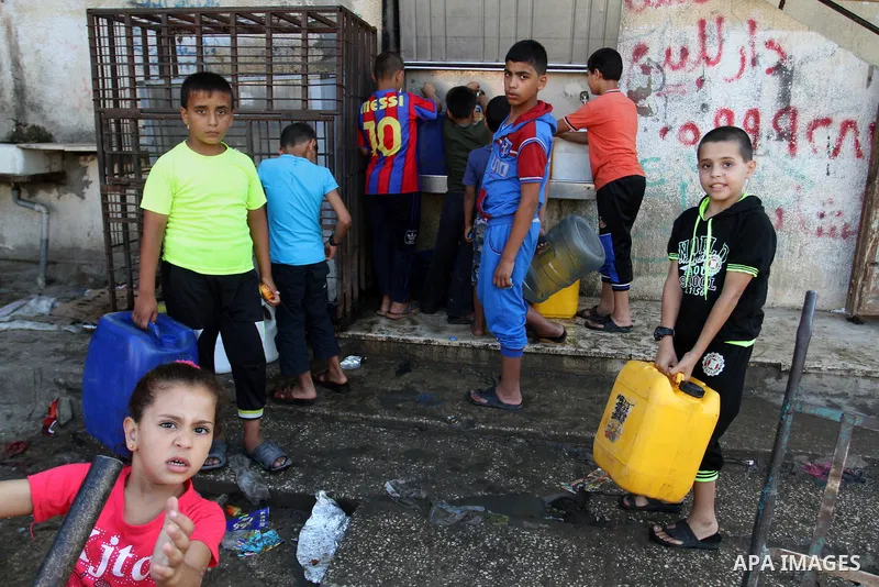 Palestinian children fill plastic bottles and jerry cans with drinking water from a public tap at the United Nations Relief and Works Agency (UNRWA) headquarters in the southern Gaza Strip refugee camp of Rafah on July 1...
