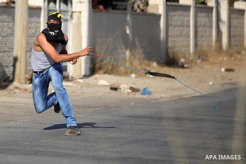 A Palestinian protester throws stones at Israeli soldiers during clashes following a protest against the construction of settlements and the confiscation of the Palestinian land, in the West Bank village of Silwad, near...