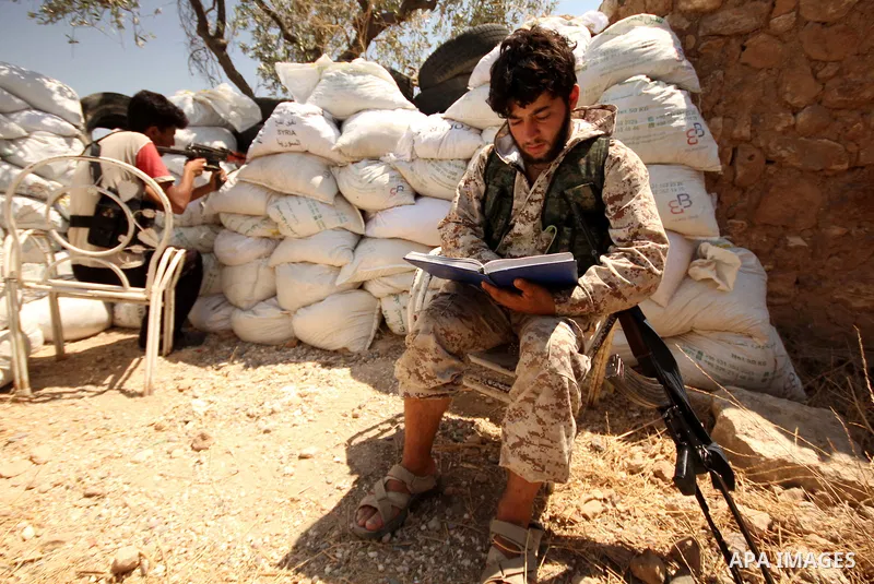 A fighter from the Free Syrian Army reads holy Quran as another takes position following clashes with the pro-regime forces, in Aziza village in the northern Syrian city of Aleppo, on July 28, 2015. Photo by Ameer al-Hal...