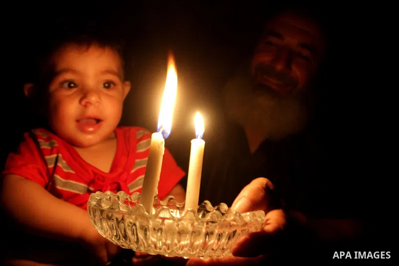 A Palestinian man sits with his grandson as he uses a candle light during a power cut in Rafah in the southern Gaza Strip, on July 28, 2015. Independent Commission for Human Rights warned Saturday of the aggravated human...
