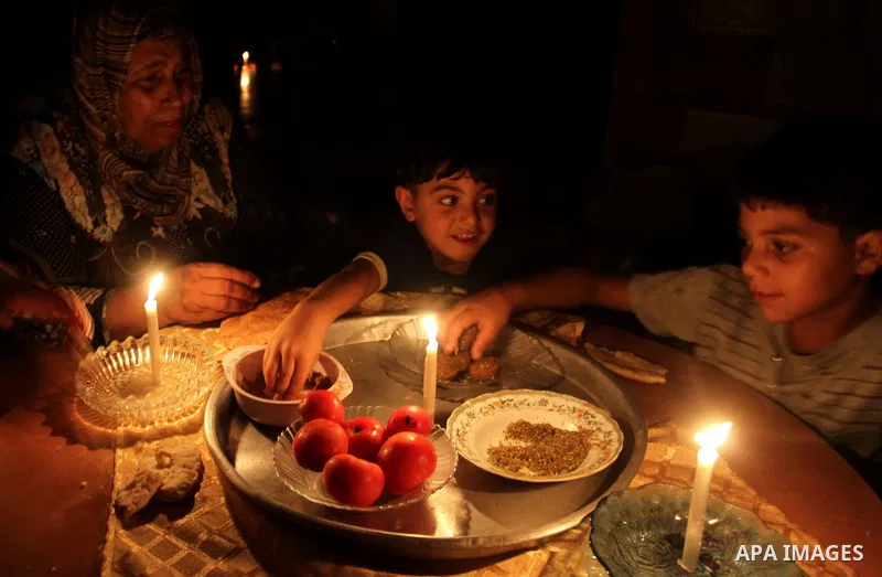 Palestinian family use a candle light as they eat dinner during a power cut in Rafah in the southern Gaza Strip, on July 28, 2015. Independent Commission for Human Rights warned Saturday of the aggravated humanitarian si...