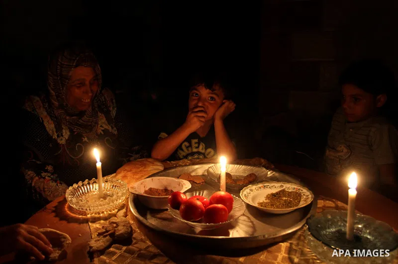 Palestinian family use a candle light as they eat dinner during a power cut in Rafah in the southern Gaza Strip, on July 28, 2015. Independent Commission for Human Rights warned Saturday of the aggravated humanitarian si...