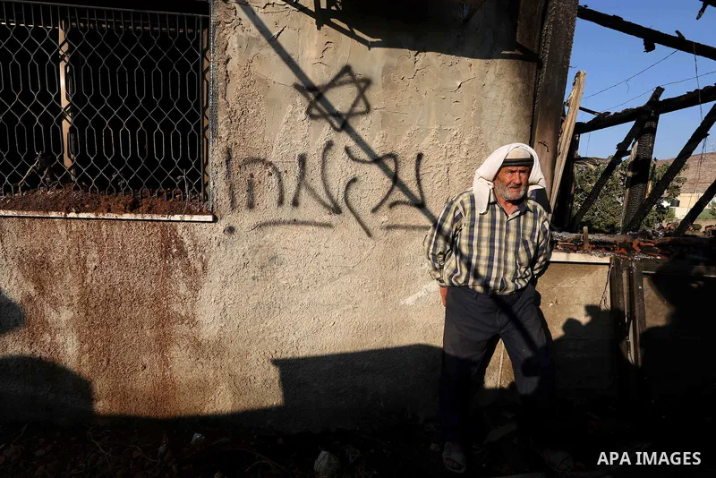 A Palestinian man walks past a graffiti reading in Hebrew 'revenge' on the wall of a house that was badly damaged from a suspected attack by Jewish extremists on two houses at Kafr Duma village near the West Bank city of...