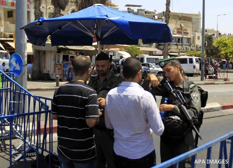 Israeli police officers chek the IDs of Muslim Palestinians as others take part in Friday noon prayers in the east Jerusalem neighbourhood of Ras al-Amud on July 31, 2015, following restrictions by Israeli police to allo...