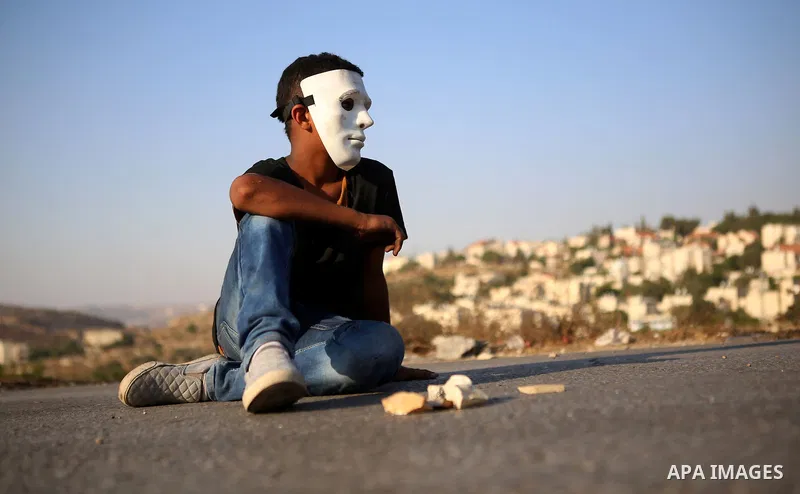 A masked Palestinian demonstrator rests on the asphalt during clashes with Israeli security forces earby the Jalazoun refugee camp and the Jewish settlement of Beit El, north of Ramallah in reaction to the death of Pales...