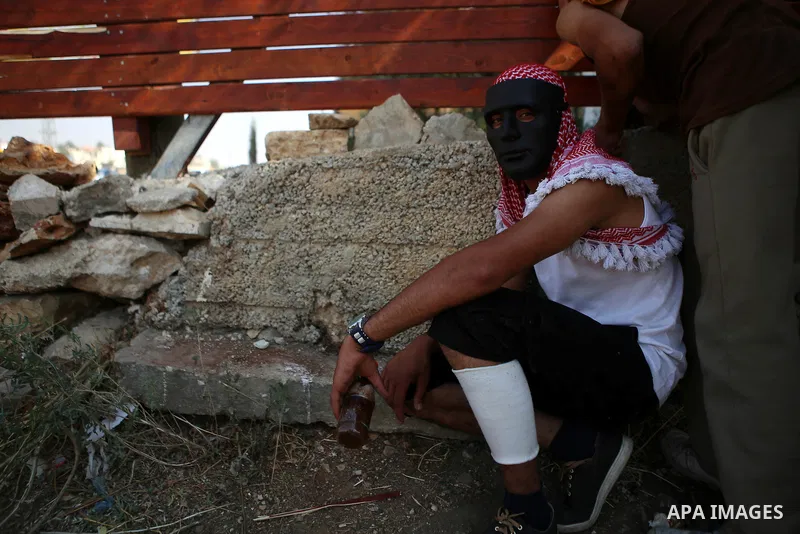 A masked Palestinian demonstrator rests during clashes with Israeli security forces earby the Jalazoun refugee camp and the Jewish settlement of Beit El, north of Ramallah in reaction to the death of Palestinian youth La...