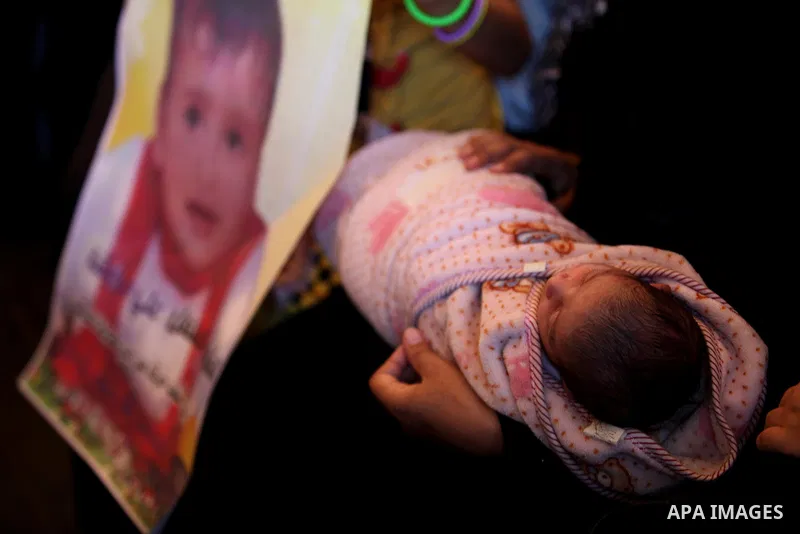 A Palestinian woman holds her child as she takes part in a protest demanding release the prisoners in Israeli jails, in front of Red cross office, in Gaza city, on on August 03, 2015. Photo by Ashraf Amra
