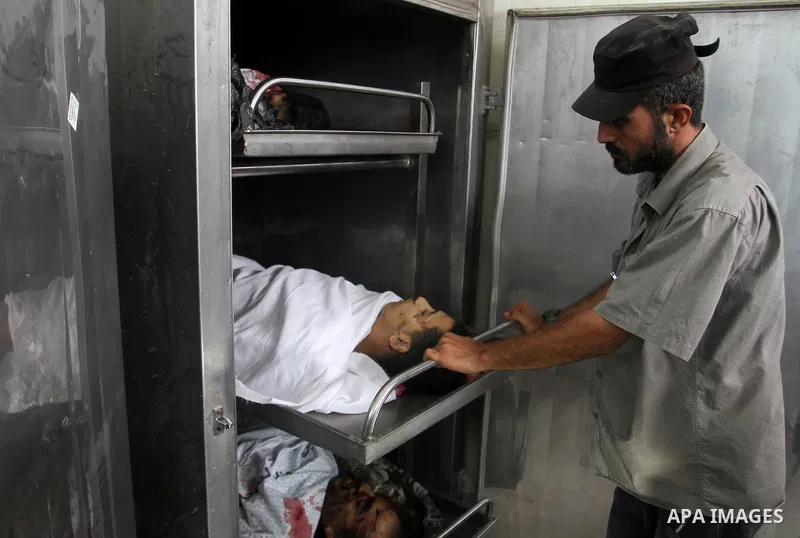 A Palestinian man stands next to four bodies lying at the morgue in the southern Gaza Strip town of Rafah following an explosion that ripped through a house in the nearby Al-Shabura refugee camp on August 6, 2015. The bl...