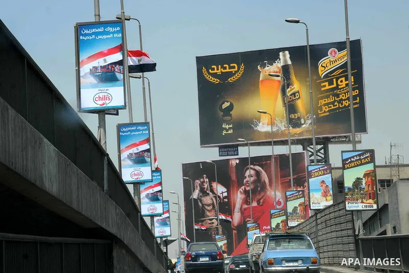 Egyptian walk past a billboard during the first day of a three days trip for the inauguration of the new Suez channel, in cairo, Egypt, Thursday, Aug. 6, 2015. Egypt is to unveil a major extension of the Suez Canal that...