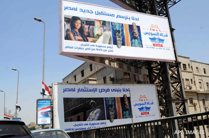 Egyptian walk past a billboard during the first day of a three days trip for the inauguration of the new Suez channel, in cairo, Egypt, Thursday, Aug. 6, 2015. Egypt is to unveil a major extension of the Suez Canal that...