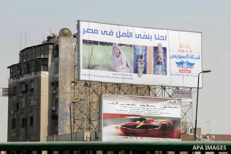 Egyptian walk past a billboard during the first day of a three days trip for the inauguration of the new Suez channel, in cairo, Egypt, Thursday, Aug. 6, 2015. Egypt is to unveil a major extension of the Suez Canal that...