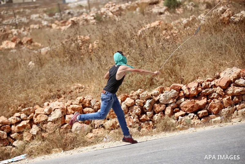 A Palestinian protester uses a sling to hurl stones at Israeli troops during clashes following a protest against Jewish settlements and the expropriation of Palestinian land in the West Bank village of Nabi Saleh, near R...