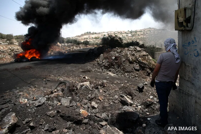A Masked Palestinian protester stands amid smoke and burning tires during clashes with Israeli security forces following a protest against the expropriation of Palestinian land by Israel in the West Bank village of Kafr...