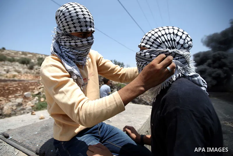 A masked Palestinian protester helps his a fellow to wear his mask during clashes with Israeli security forces following a protest against the expropriation of Palestinian land by Israel in the West Bank village of Kafr...