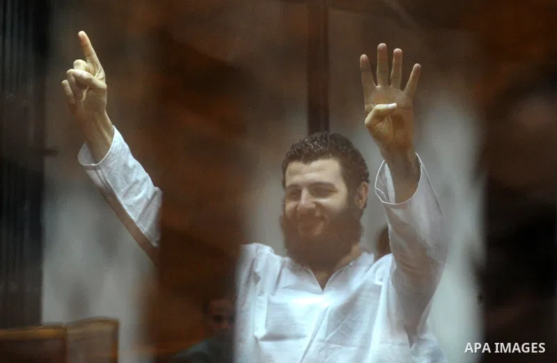 An Egyptian Muslim Brotherhood defendant waves as he stands behind the bars during his trial, along with ousted Islamist president Mohamed Morsi (unseen), in a court in Cairo on August 8, 2015. Cairo Criminal Court resum...